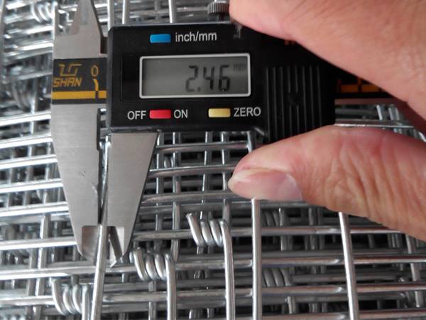 A worker is testing the wire diameter of field fencing.